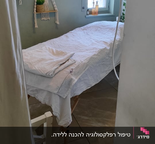חדר טיפולים עם מיטת עיסוי ומוצרים על אדן החלון